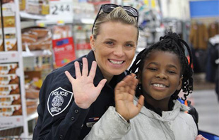 a staunton police officer and child wave at the camera during the shop with a cop event