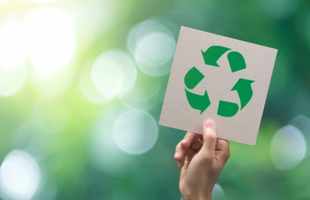 A hand holding a card with the three-arrow recycling symbol on it in green