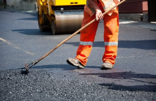 A man is pictures using a rake to pave a street